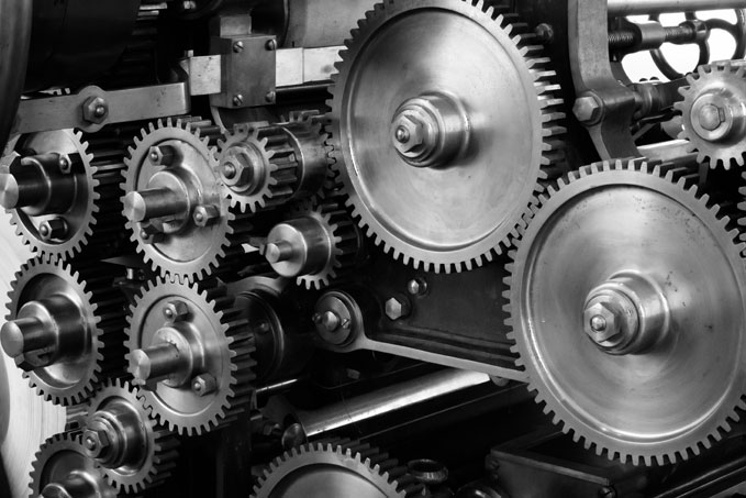 Nahaufnahme mehrerer ineinandergreifender Metallzahnräder und -räder in einem komplexen mechanischen System, das komplizierte Maschinenbau- und Industriemaschinenkomponenten in Schwarzweiß zeigt. - RUF Beratung - Ihre Contact Center Berater