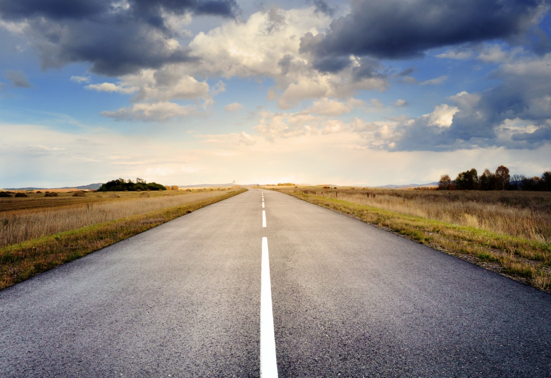 Eine gerade, leere Straße erstreckt sich in der Ferne durch flache Felder unter einem teilweise bewölkten Himmel, durch den das Sonnenlicht bricht – die perfekte visuelle Metapher für eine klare Customer Journey-Spezifikation, die sich vor uns entfaltet. - RUF Beratung - Ihre Contact Center Berater