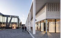 Modernes Outdoor-Einkaufszentrum mit großen Glasfassaden für Etro und Burberry. Die Menschen flanieren auf breiten, von hohen weißen Säulen und Backsteinmauern gesäumten Wegen unter klarem Himmel, während Dienstleister-Steuerung für ein reibungsloses Facility Management sorgt. - RUF Beratung - Ihre Contact Center Berater