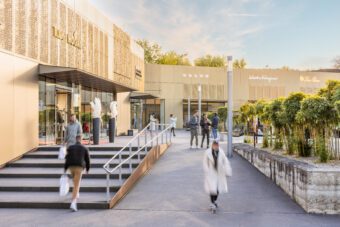 An einem klaren Tag schlendern Menschen durch ein exklusives Einkaufszentrum mit moderner, goldfarbener Architektur, viel Grün und reibungsloser Dienstleister-Steuerung, in dem sich Luxusgeschäfte wie Louis Vuitton und Salvatore Ferragamo befinden. - RUF Beratung - Ihre Contact Center Berater