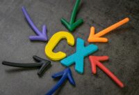 Bunte Pfeile zeigen auf die Holzbuchstaben C und X auf dunklem Hintergrund und symbolisieren das Konzept der Continuous Experience (CX) in der Kundeninteraktion. - RUF Beratung - Ihre Contact Center Berater
