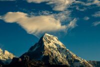 Ein schneebedeckter Berggipfel erhebt sich steil unter einem tiefblauen Himmel, über dem links vom Gipfel eine große, dünne weiße Wolke schwebt – eine wahre Inspiration für Peak Management. - RUF Beratung - Ihre Contact Center Berater