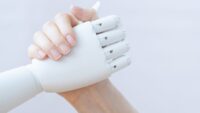 Zwei Hände die sich die Hand geben. Die eine Hand ist eine MEnschenhand. Die andere die eines Roboters.